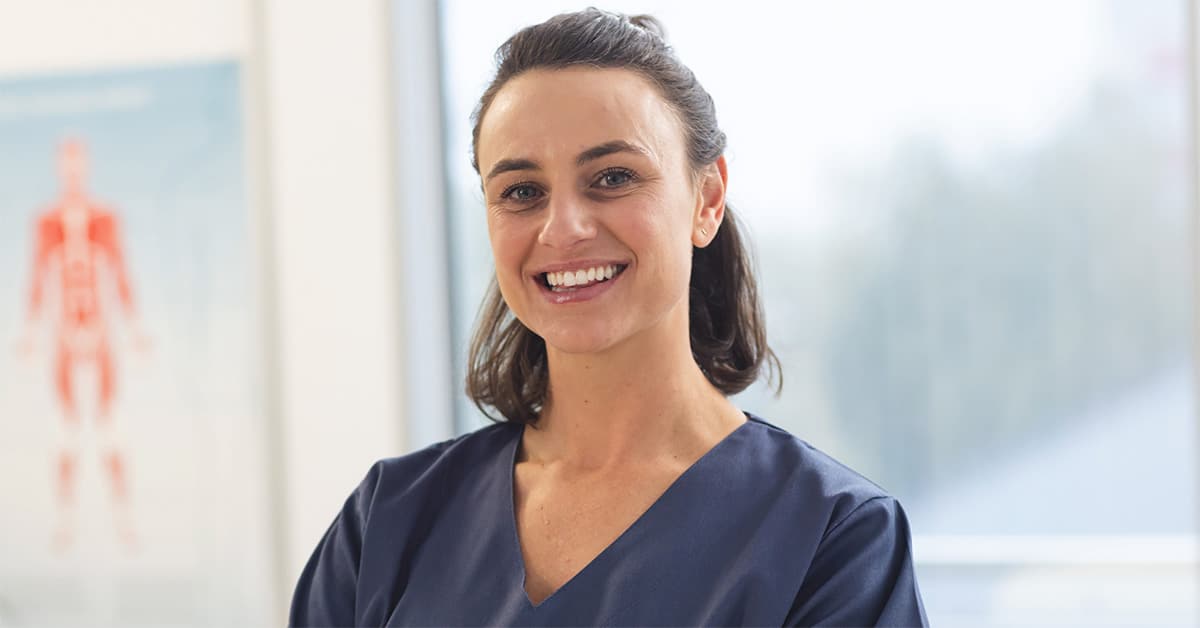 CORU Registered Female Phsyiotherapist standing smiling in a clinic wearing navy scrubs